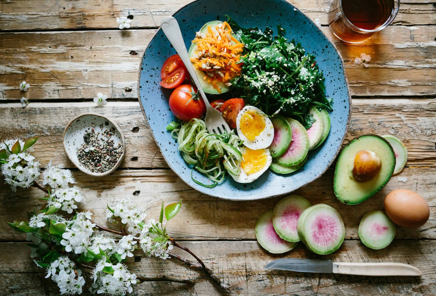 Prato com abacate, ovos, legumes e folhas sobre uma mesa de madeira