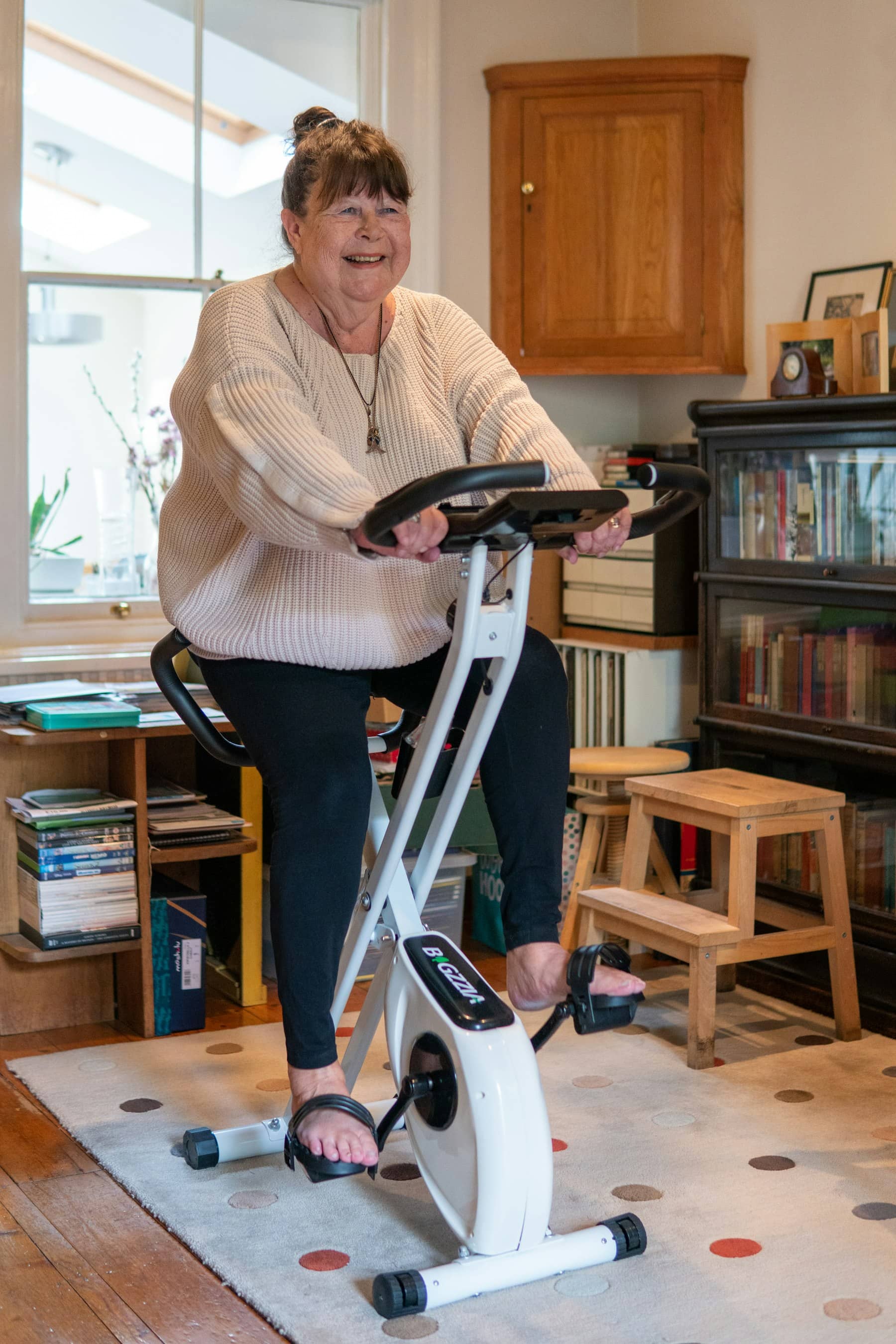 Mulher sorrindo enquanto pedala uma bicicleta ergométrica em casa